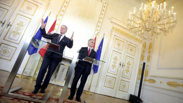 Zwei Männer stehen an Rednerpulten vor Flaggen in einem prunkvollen Raum.