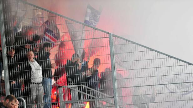 Fußballfans zünden Pyrotechnik hinter einem Zaun im Stadion.
