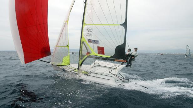 Zwei Segler steuern ein Segelboot mit rotem Spinnaker auf dem Meer.