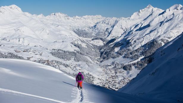 Eine Skifahrerin fährt auf einer schneebedeckten Piste in Richtung eines Alpendorfes.