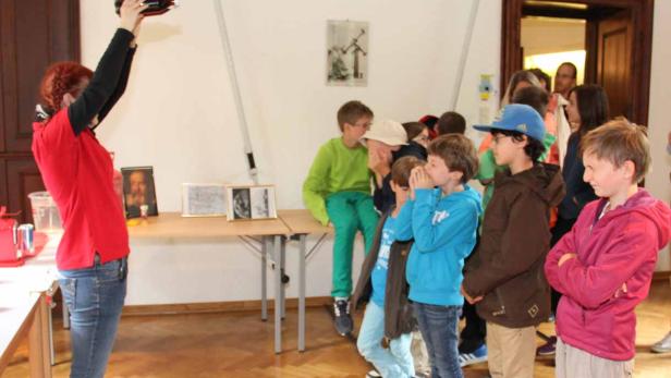 Eine Frau demonstriert vor einer Gruppe von Kindern ein Experiment mit einer Flasche.