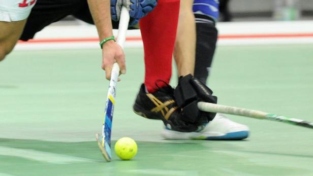 Zwei Hockeyspieler mit Schlägern und einem gelben Ball auf dem Spielfeld.