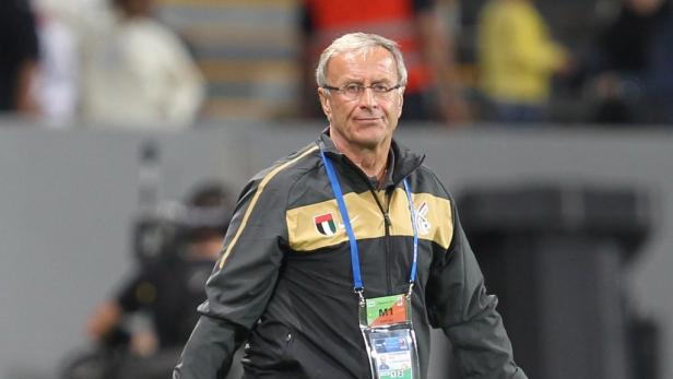 Ein Mann mit Brille und Trainingsjacke steht auf einem Sportplatz.