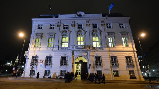 Das Bundeskanzleramt in Wien bei Nacht mit Menschen vor dem Eingang.