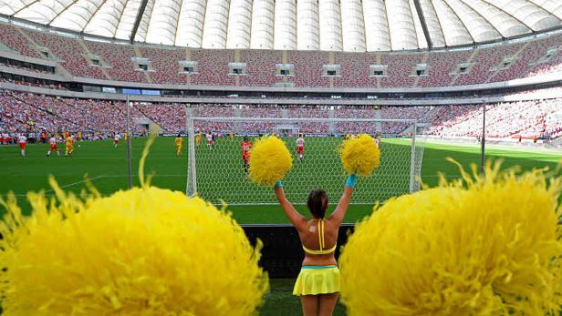 Eine Cheerleaderin feuert ein Fußballspiel mit gelben Poms an.