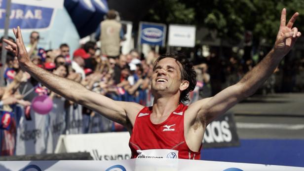Ein Marathonläufer überquert mit erhobenen Armen die Ziellinie.