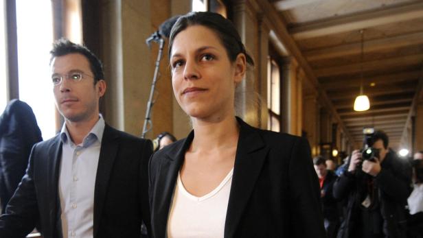 Laura Rudas Zwei Personen in Anzügen gehen durch einen Flur, während Fotografen Fotos machen.