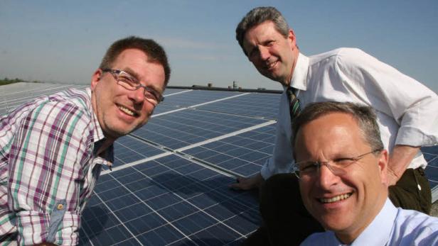 Drei Männer stehen vor einer Reihe von Solarmodulen und lächeln.