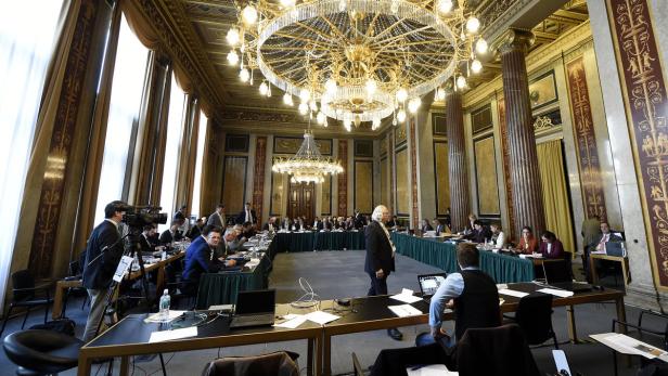 Ein großer Konferenzraum mit einem langen Tisch und vielen Teilnehmern unter einem Kronleuchter.