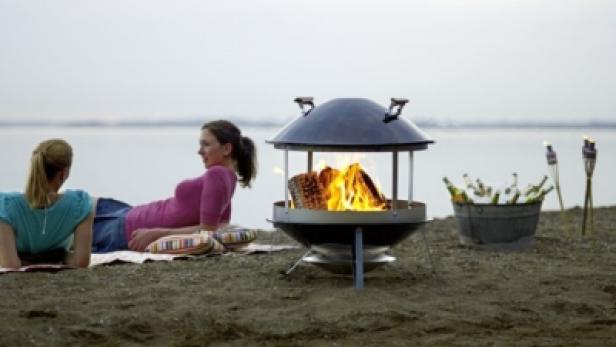 Zwei Frauen entspannen am Strand neben einem Lagerfeuer in einer Feuerschale.