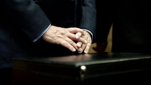 Ein Mann im Anzug mit gefalteten Händen auf einem Tisch.