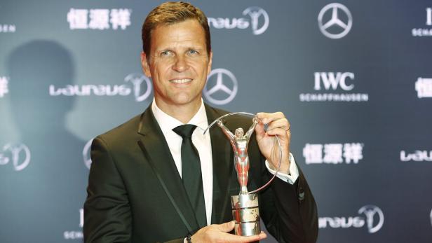 Oliver Bierhoff posiert mit einer Laureus-Statue vor einem grauen Hintergrund.