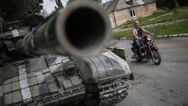 Ein Mann fährt auf einem roten Motorrad an einem Panzer vorbei.