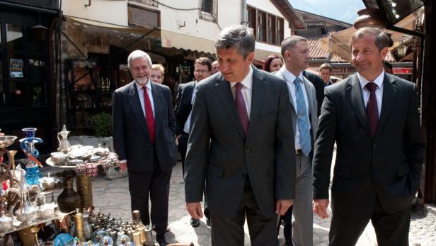 Eine Gruppe von Männern in Anzügen geht durch eine belebte Straße mit Souvenirläden.