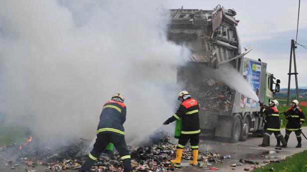 Feuerwehrleute löschen einen brennenden Müllwagen auf einer Landstraße.