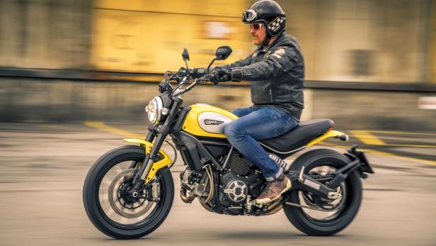 Ein Mann fährt eine gelbe Ducati Scrambler mit Helm und Schutzbrille.