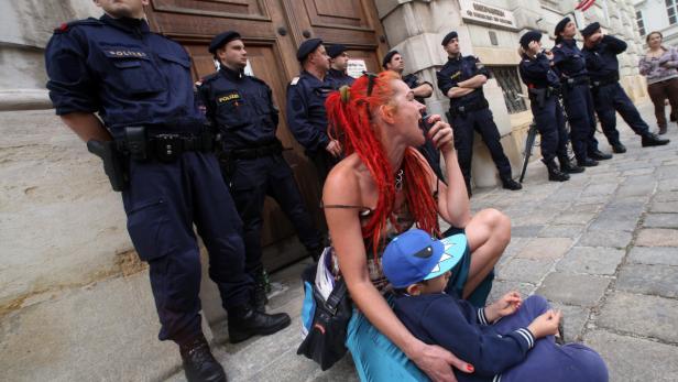 Eine Frau mit roten Dreads sitzt mit einem Kind vor einer Reihe Polizisten.