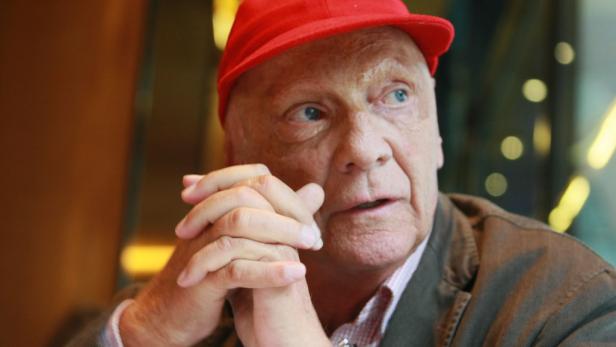 Niki Lauda mit roter Kappe, die Hände vor dem Gesicht verschränkt.