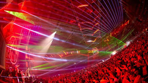 Eine große Menschenmenge jubelt bei einem Konzert mit roter Beleuchtung und Lasershow.