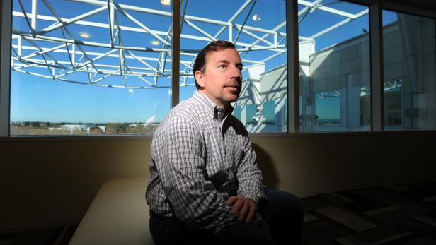 Ein Mann sitzt vor einem großen Fenster mit Blick auf eine Stadt.