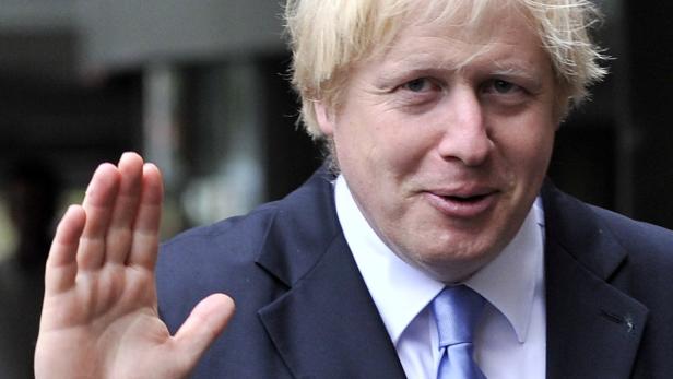 Boris Johnson winkt in einem dunklen Anzug.