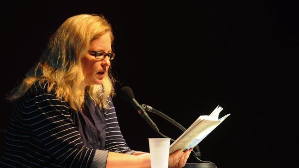 Eine Frau mit Brille liest aus einem Buch vor einem Mikrofon.