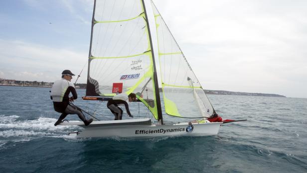 Zwei Segler steuern ein Segelboot mit der Aufschrift „EfficientDynamics“ auf dem Meer.