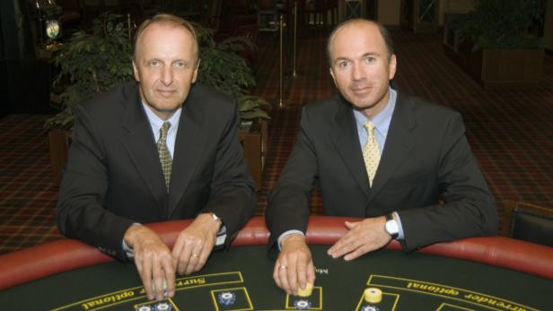 Zwei Männer im Anzug sitzen an einem Pokertisch und spielen mit Jetons.