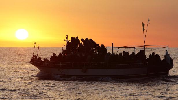 Ein Boot mit vielen Menschen fährt bei Sonnenuntergang auf dem Meer.