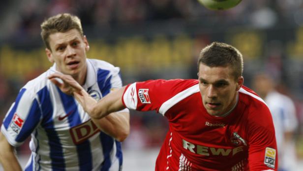 Zwei Fußballspieler während eines Spiels, einer im roten Trikot, der andere im blau-weiß gestreiften Trikot.