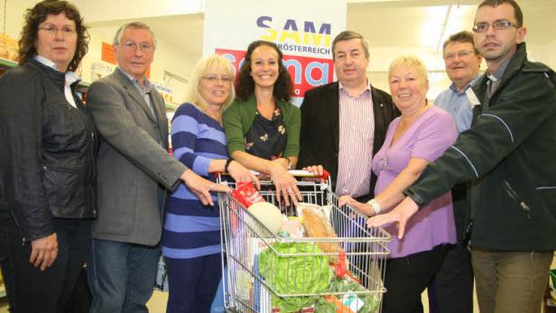 Eine Gruppe von Personen steht um einen Einkaufswagen voller Lebensmittel.