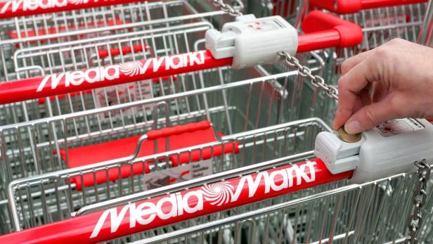 Eine Hand führt eine Münze in den Pfandschloss eines Einkaufswagens von Media Markt ein.