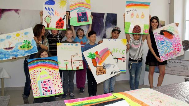 Eine Gruppe von Kindern und zwei Frauen präsentieren stolz ihre bunten Gemälde.