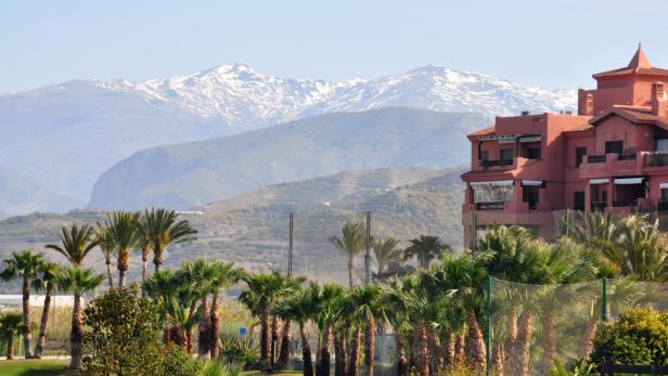 Ein rosafarbenes Gebäude mit Palmen im Vordergrund und schneebedeckten Bergen im Hintergrund.