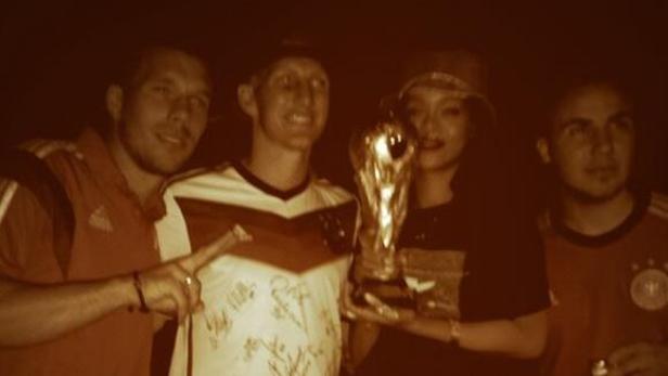 Rihanna posiert mit deutschen Fußballspielern und dem WM-Pokal.