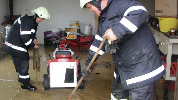 Zwei Feuerwehrleute beseitigen mit einem Schieber und einem Tuch eine Überschwemmung in einem Gebäude.