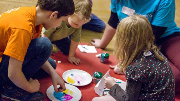 Eine Gruppe Kinder sitzt auf dem Boden und bastelt mit Farben und Papier.