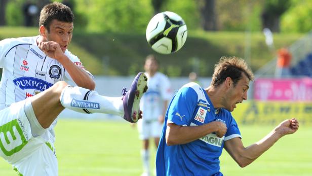 Ein Fußballspieler schießt den Ball, während ein anderer Spieler sich duckt.