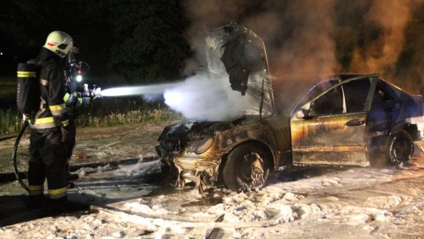 Ein Feuerwehrmann löscht ein brennendes Auto mit einem Wasserstrahl.
