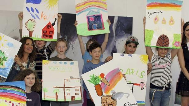 Eine Gruppe von Kindern und eine Frau präsentieren stolz ihre selbstgemalten Bilder.