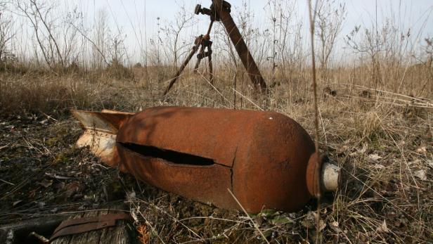 Eine rostige, beschädigte Bombe liegt in einem Feld mit trockenem Gras.