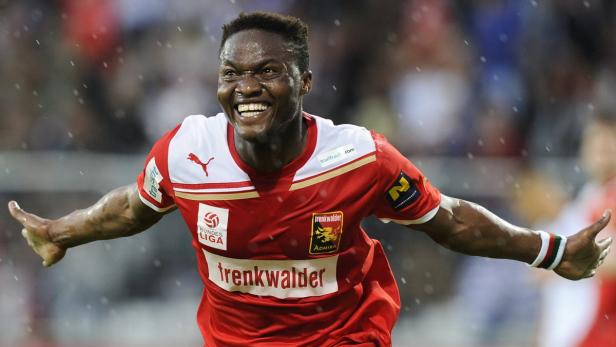 Ein lächelnder Fußballspieler im roten Trikot mit ausgebreiteten Armen.