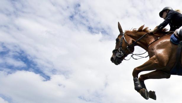 Ein Reiter springt mit seinem Pferd vor einem Himmel mit Wolken.