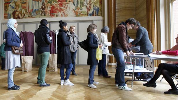 Menschen stehen in einer Schlange vor Wahlkabinen in einem Raum mit einem Wandgemälde.