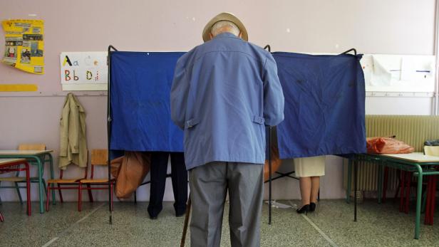 Ein älterer Mann mit Hut wählt in einer Wahlkabine.
