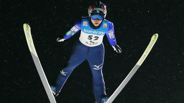 Eine Skispringerin in blauer Wettkampfkleidung während eines Sprungs.