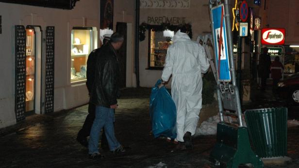 Ein Mann in einem Schutzanzug trägt einen blauen Sack an einer dunklen Straße entlang.