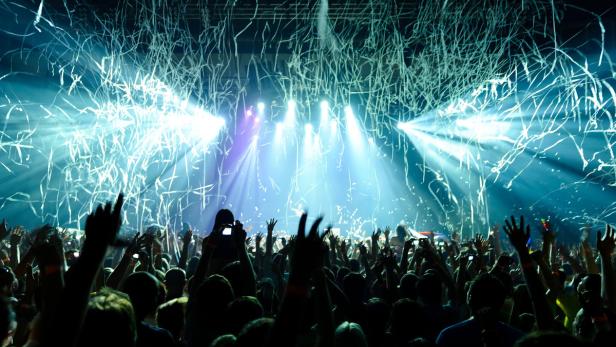 Eine Menschenmenge feiert mit Konfetti und erhobenen Händen auf einem Konzert.