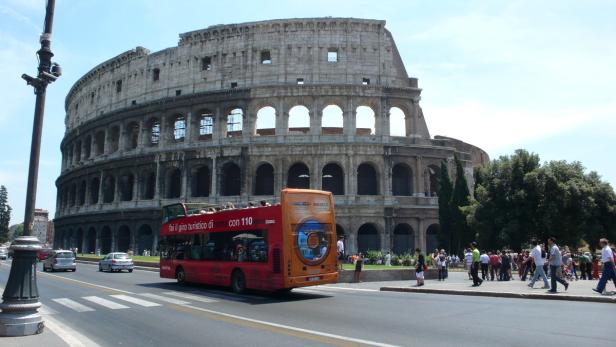 Ein roter Doppeldeckerbus fährt vor dem Kolosseum in Rom.