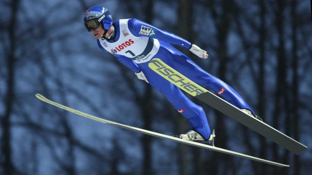 Ein Skispringer in blauem Anzug während eines Sprungs.